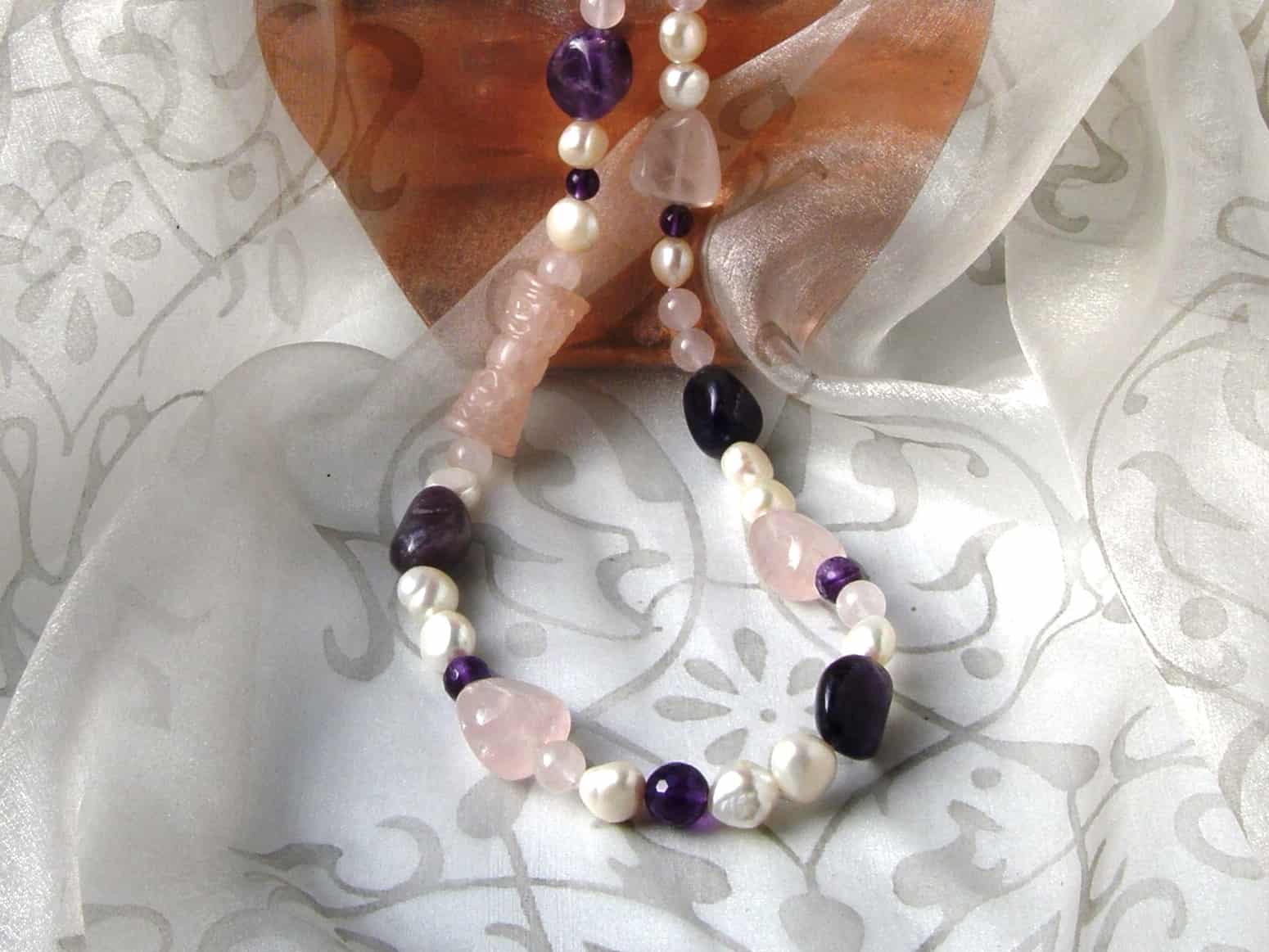 Freshwater Pearl Necklace designed with pebble shaped Amethyst, Rose Quartz in an asymmetrical pattern and featuring a carved Rose Quartz cylinder. The Necklace is finished with an Oval shape Sterling Silver Clasp.