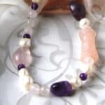 Freshwater Pearl Necklace designed with pebble shaped Amethyst, Rose Quartz in an asymmetrical pattern and featuring a carved Rose Quartz cylinder. The Necklace is finished with an Oval shape Sterling Silver Clasp.