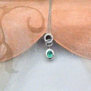 Dainty Emerald Diamond Pendant set with oval Emerald and circles of white gold pave set with diamonds, worn on a fine belcher chain in 18ct White Gold. The Isla Emerald is a bright green with lighter colour flashes within a bezel setting. Emerald Weight 0.36 carats;   Diamond Weight 0.08 carats. Pendant length 19mm. 