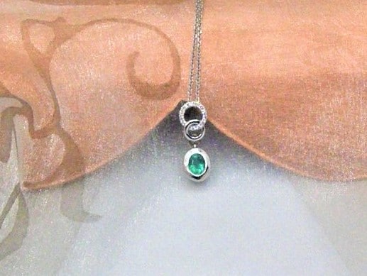 Dainty Emerald Diamond Pendant set with oval Emerald and circles of white gold pave set with diamonds, worn on a fine belcher chain in 18ct White Gold. The Isla Emerald is a bright green with lighter colour flashes within a bezel setting. Emerald Weight 0.36 carats;   Diamond Weight 0.08 carats. Pendant length 19mm. 